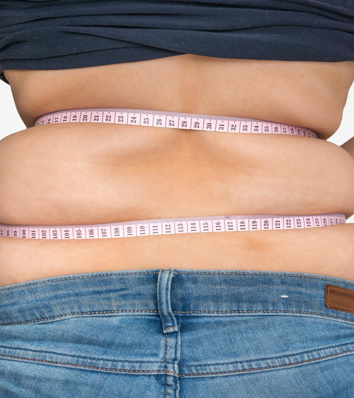 A lady measuring her belly size using a measuring tape